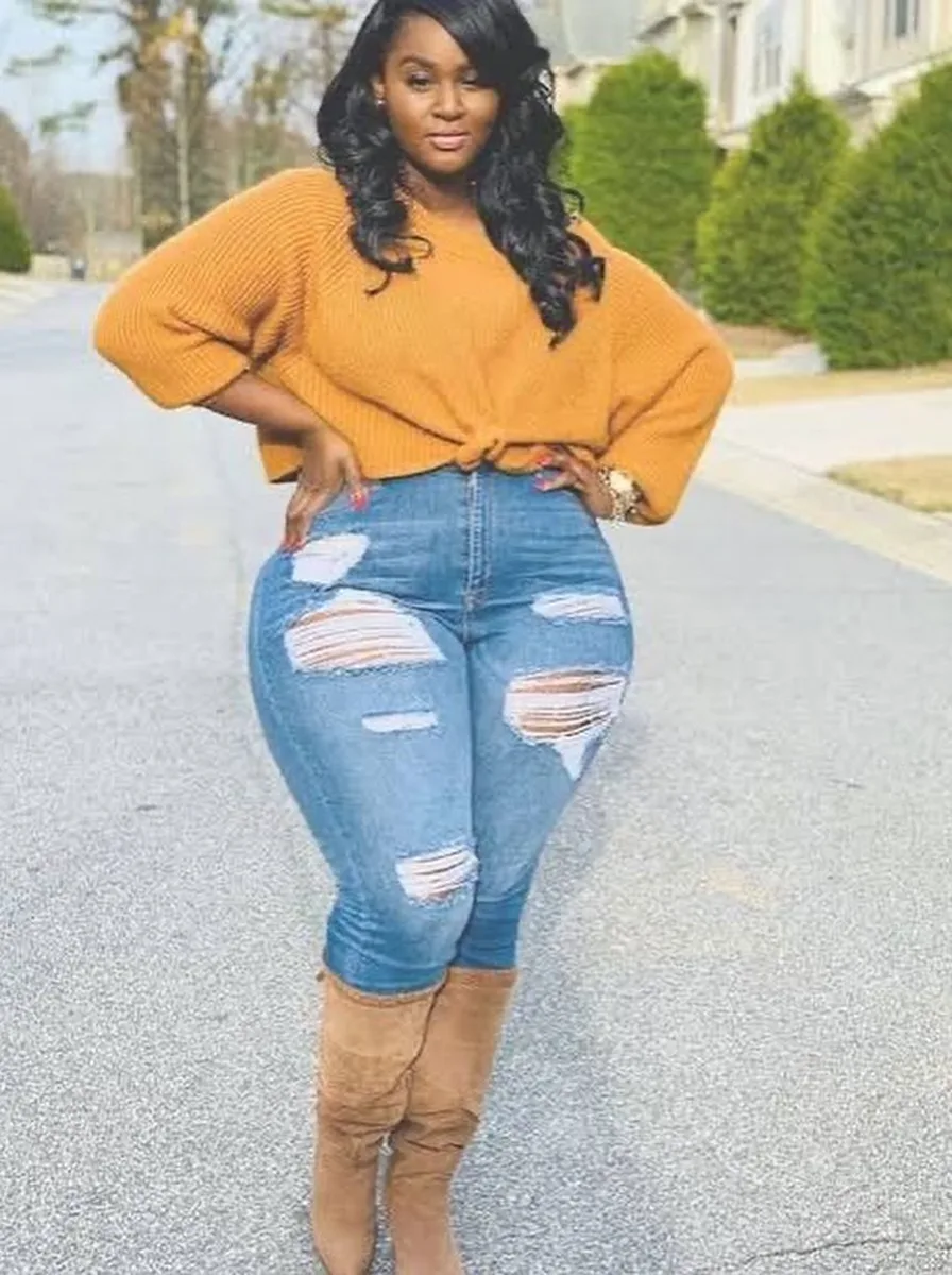 Plus size woman wearing a mustard front-tie knit sweater with ripped jeans and tan over-the-knee boots