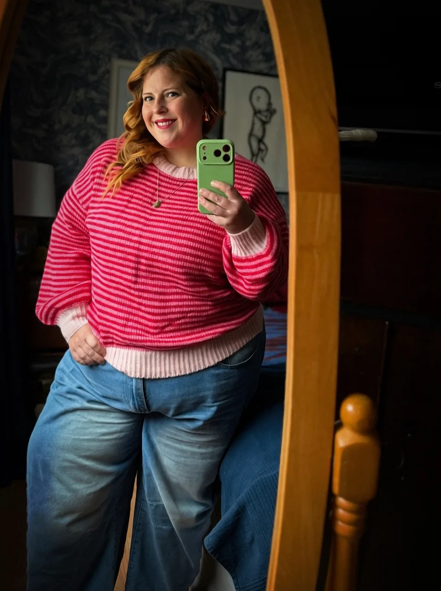 Plus size woman wearing a pink and red striped sweater with blue wide-leg jeans