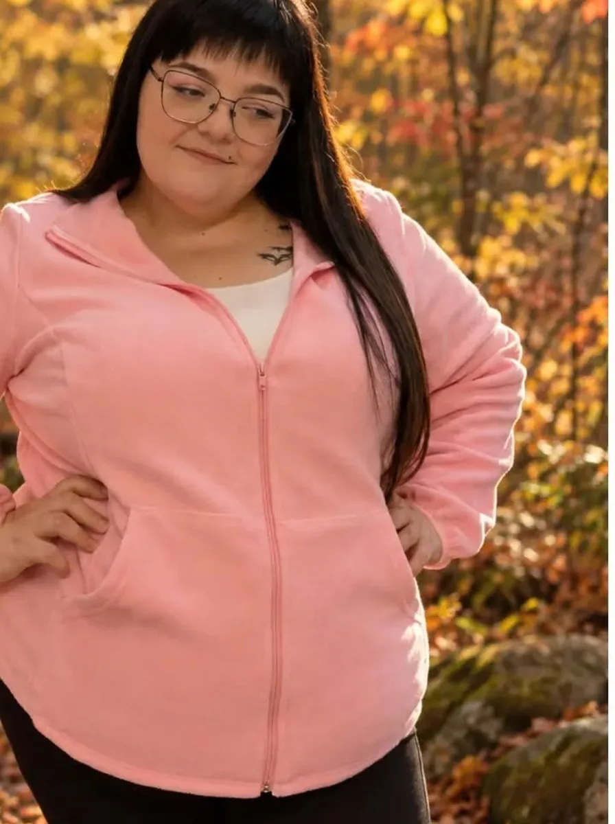 Plus size woman wearing a pink zip fleece jacket with black leggings in an autumn forest