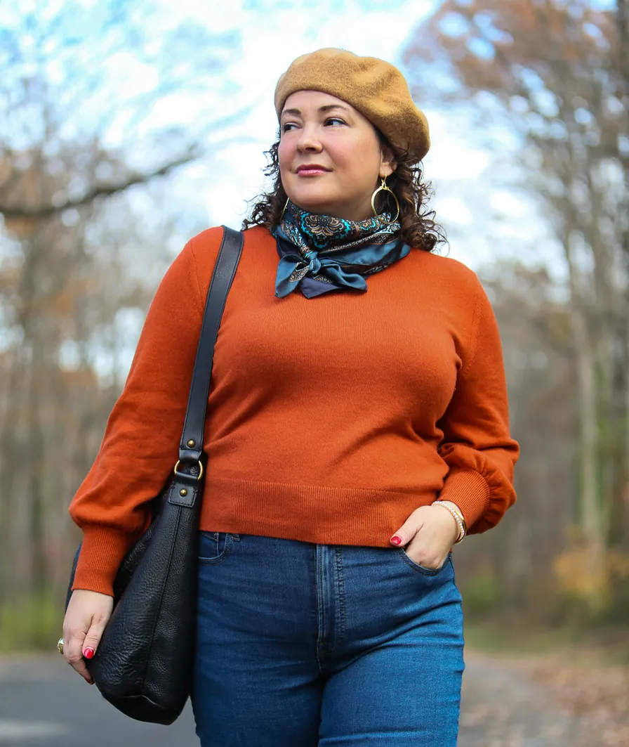 Plus-size woman in a rust sweater, camel beret, paisley scarf, and dark jeans